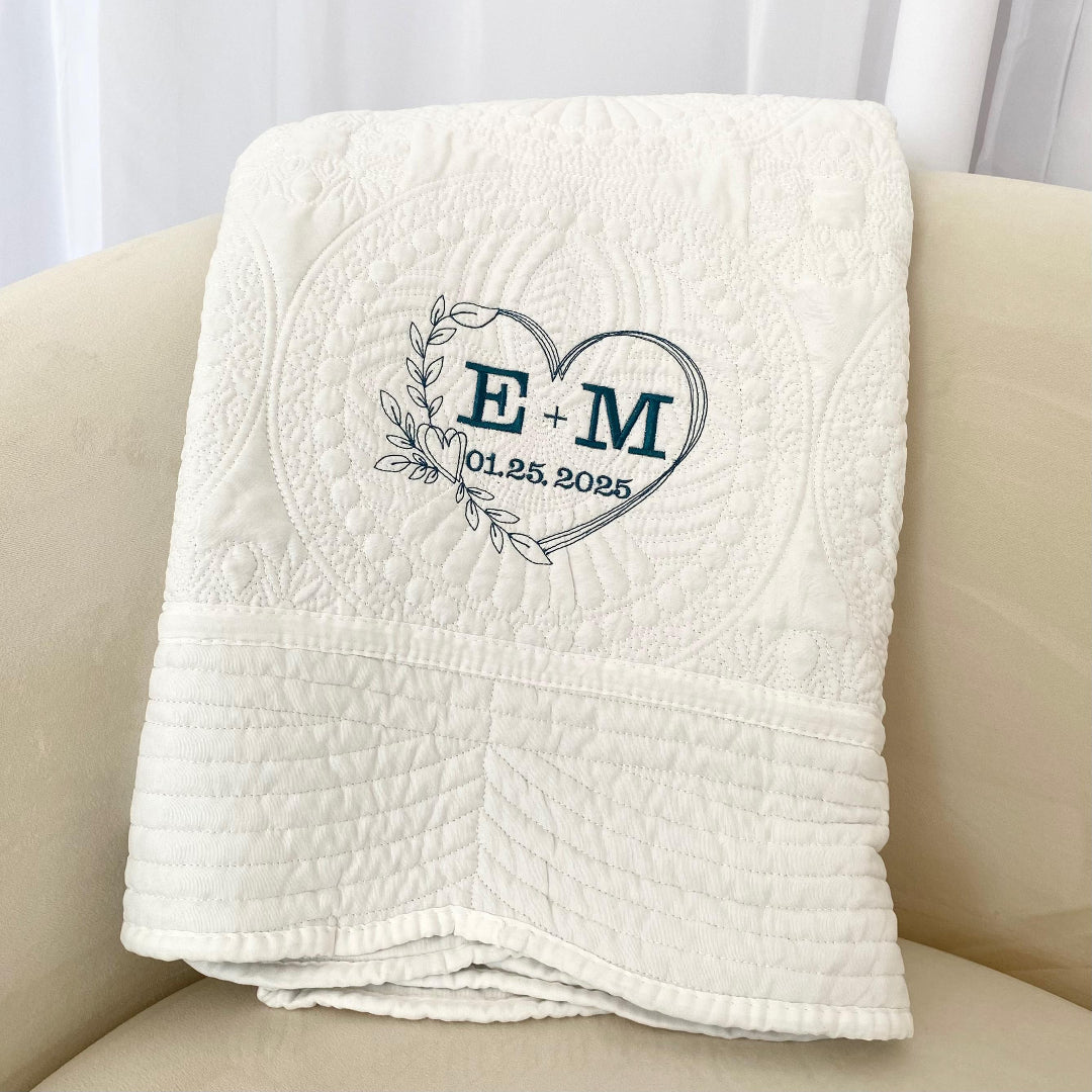 White quilt with embroidered initials and date wedding on a beige chair